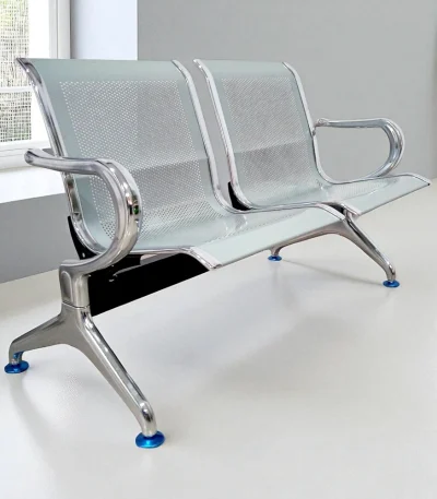 Chrome-finish 2 seater metal waiting chair with perforated design placed in a modern room with white flooring and window view